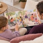 Wenn Kinder fragen: „Warum ist das so?“ Eine erwachsene Person und ein Kind betrachten auf dem Sofa ein Bilderbuch mit Illustrationen von Menschen mit unterschiedlichen Hilfsmitteln.